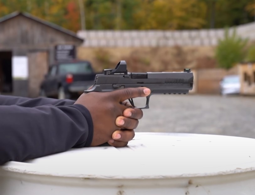 two black hands holding a handgun with a red dot sight attached